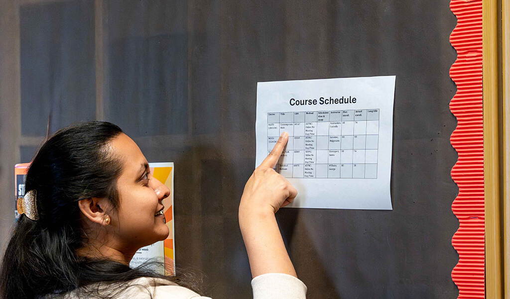 Graduate student pointing to a course schedule posted on a pin board