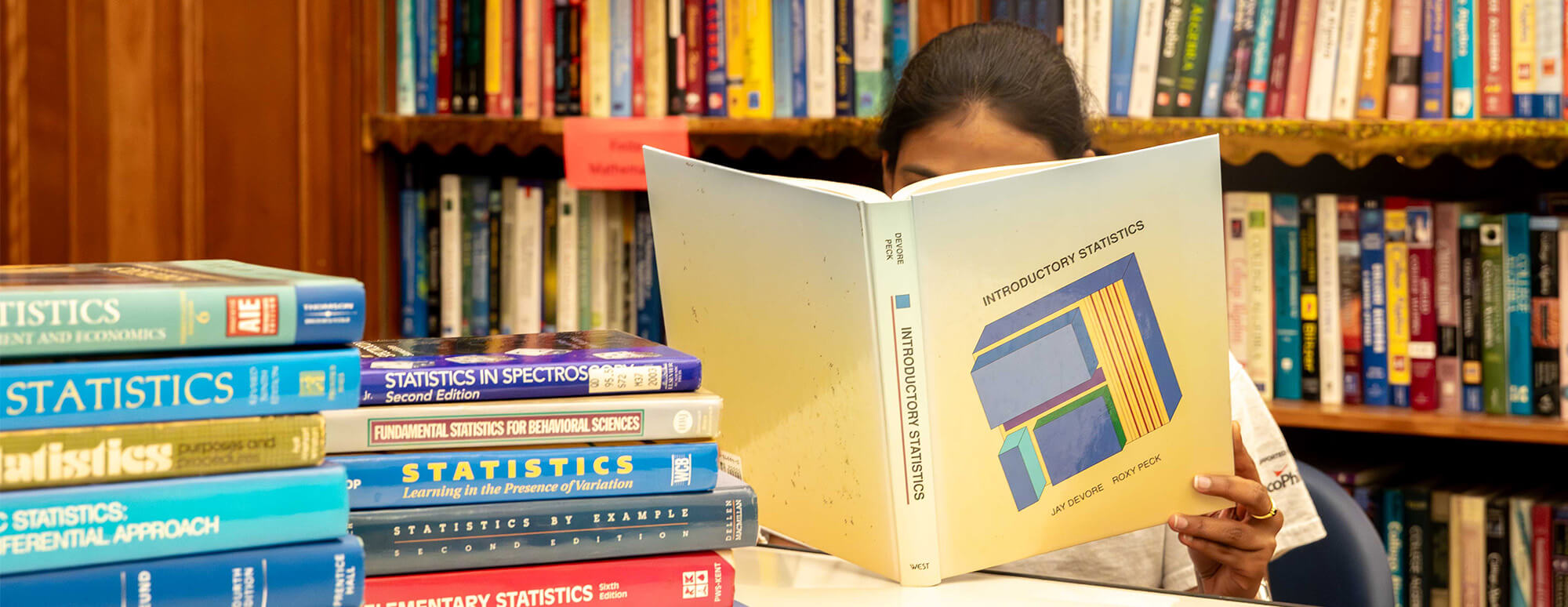 Department tutor sitting at a desk with books on it in the tutoring center