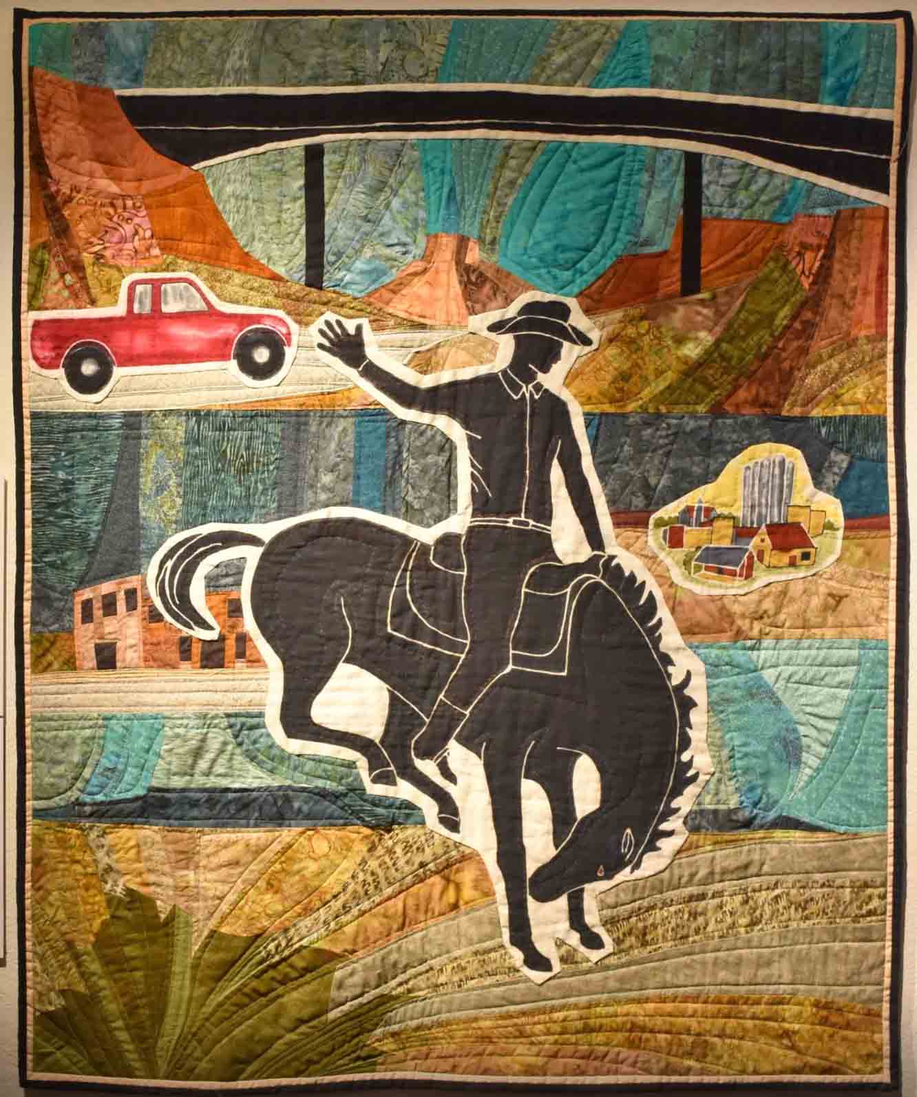 Art quilt in west Texas colors with cowboy on bucking bronco horse and red pick up truck