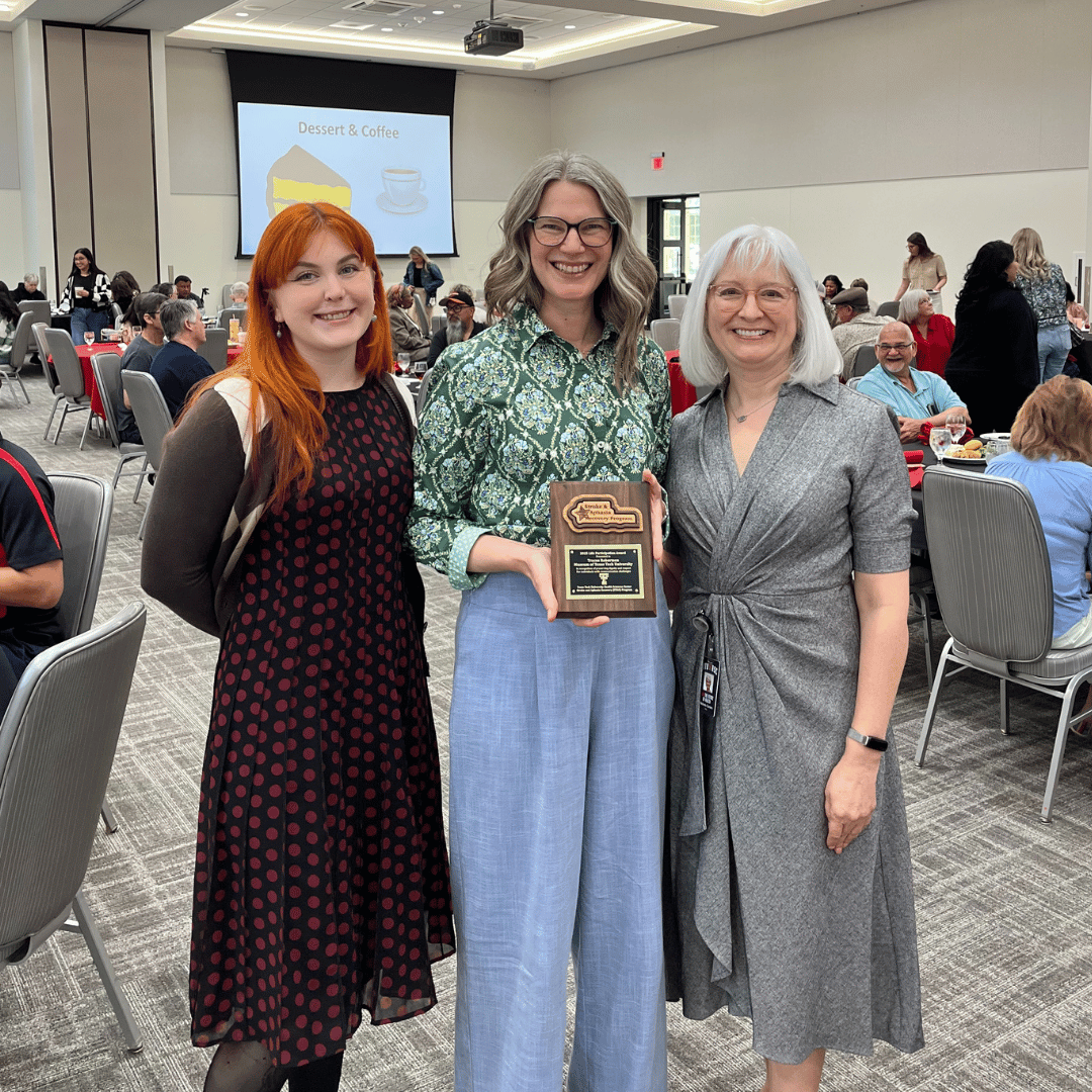 Tracee Robertson, Tess Drake, and Melinda Corwin standing holding the Award