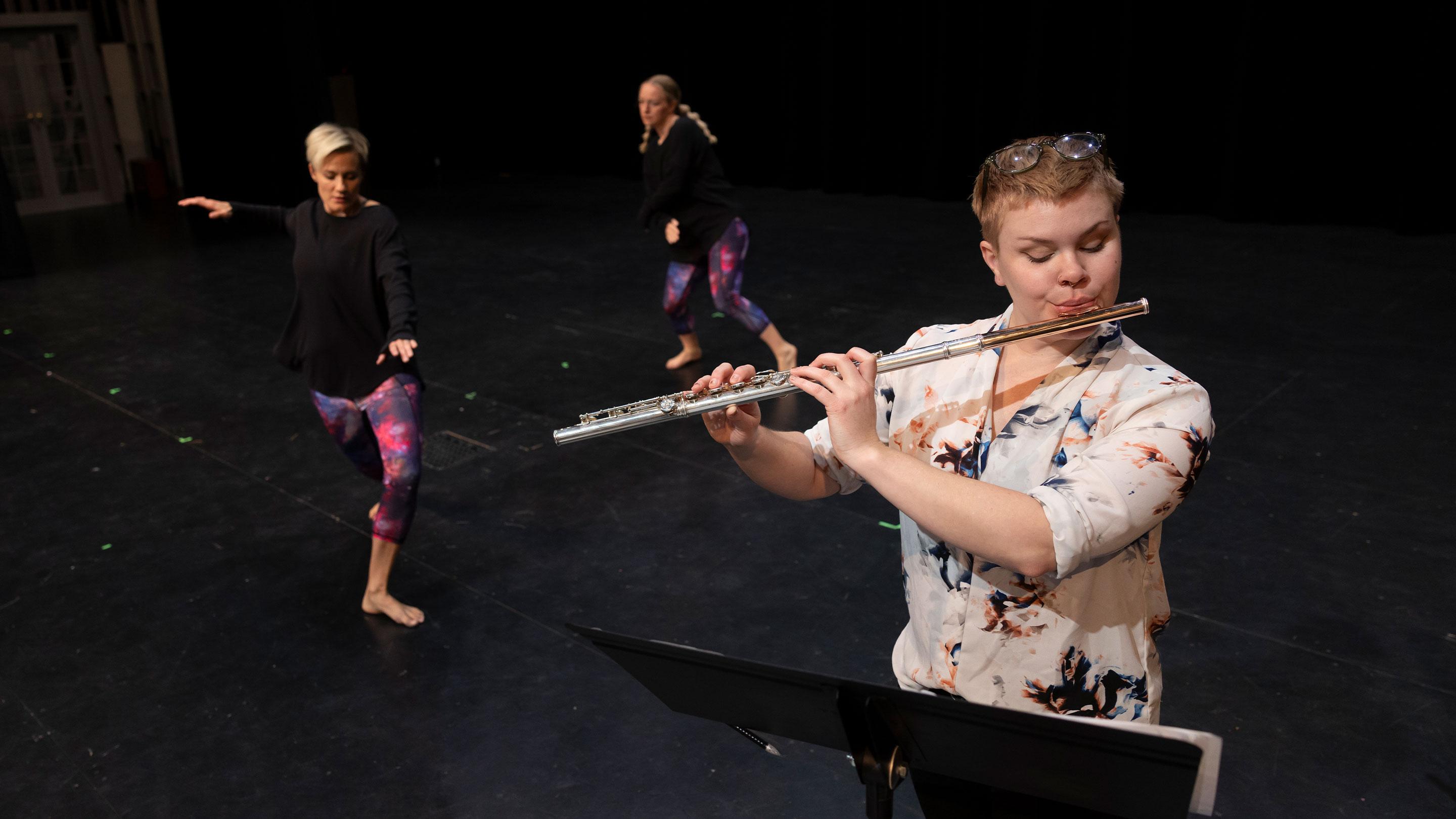 student plays flute while two students dance
