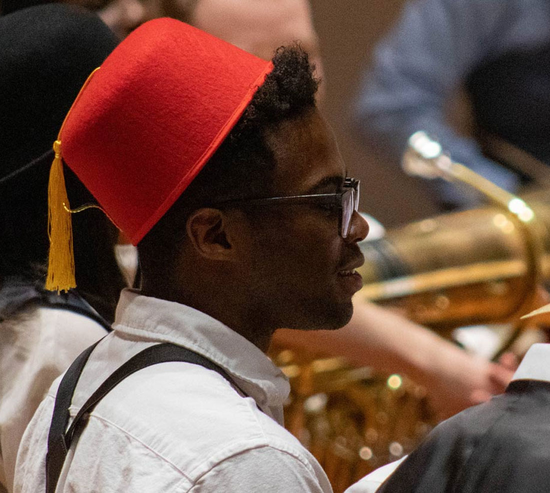Student in fez hat on stage with orchestra