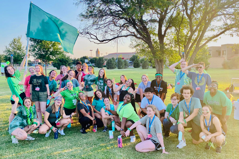 Group of kids sitting in the park under a green flag