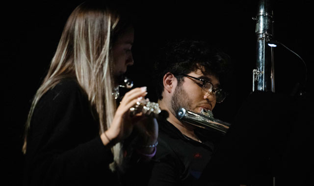 Students playing flute in front of a microphone