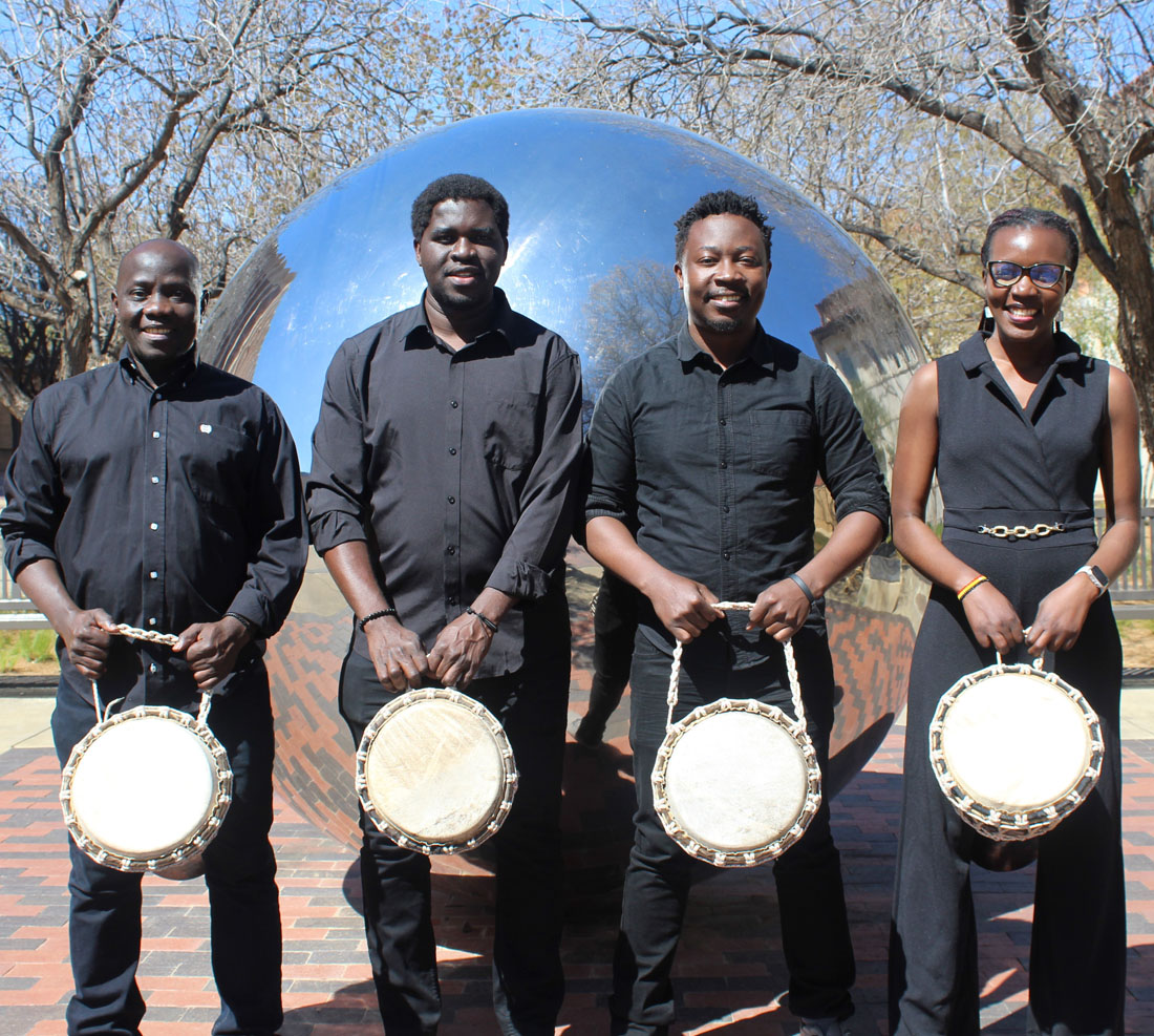 4 students in front of library holding a drum