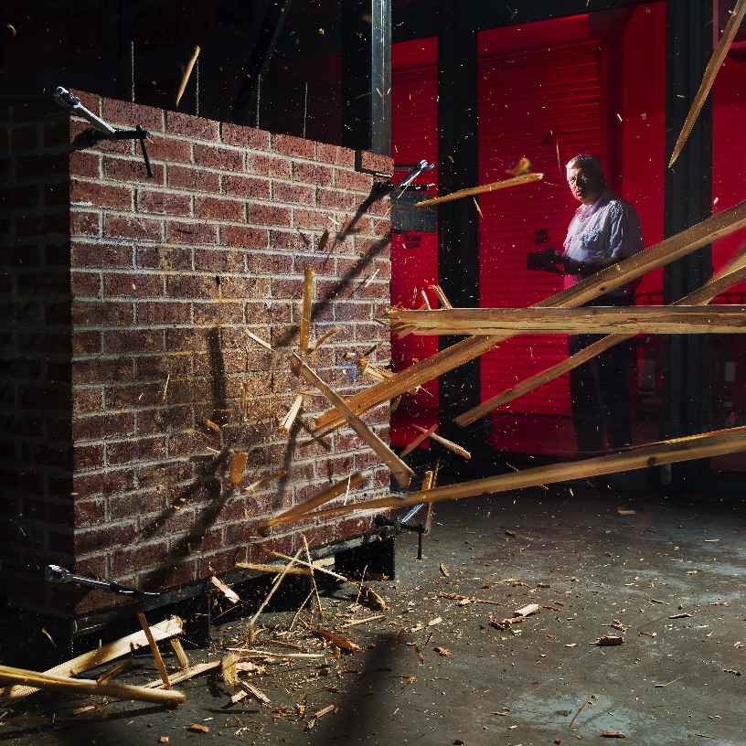 Board crashing against wall, with pieces of board flying during a test at the Debris Impact Facility.