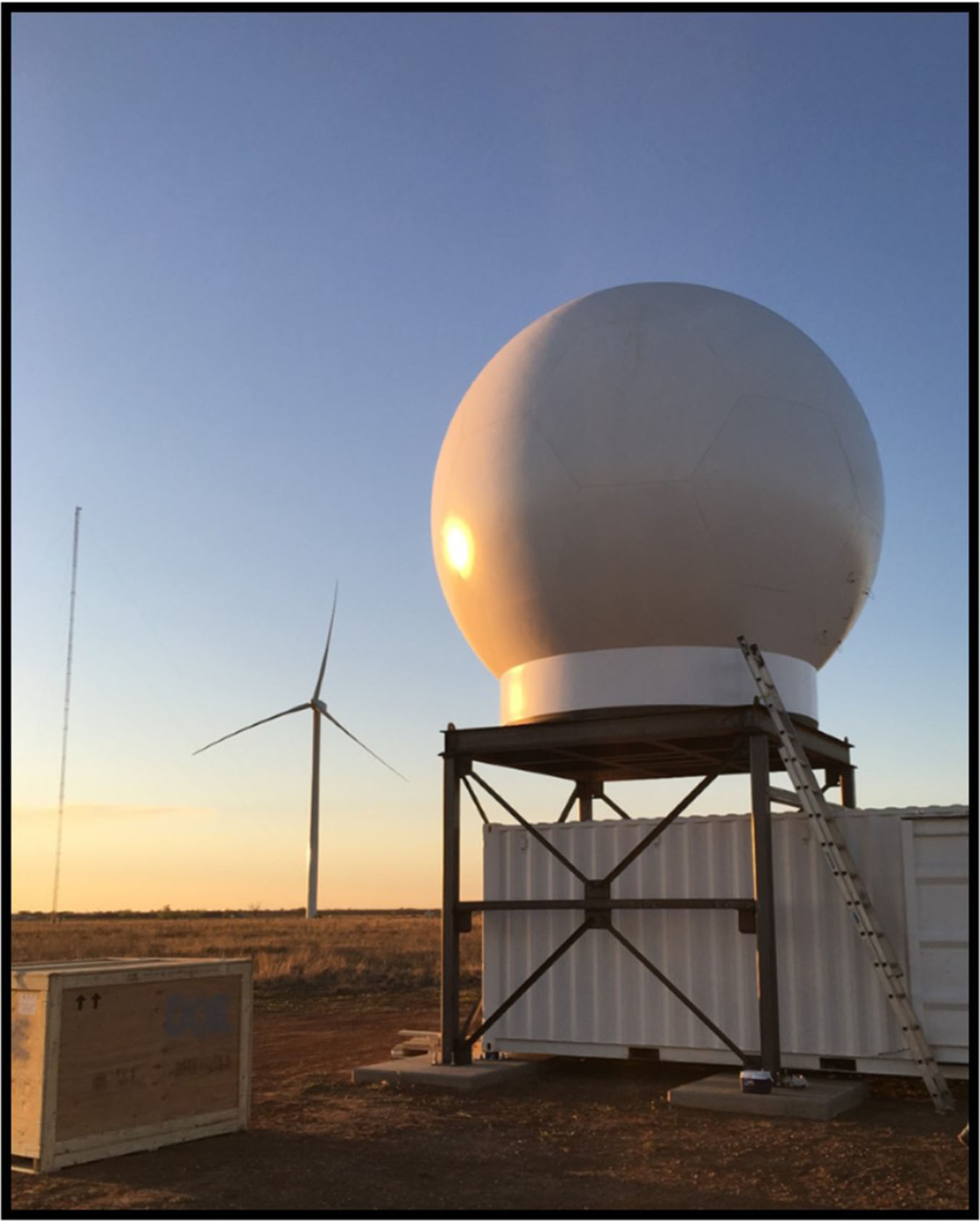 Weather radar in the field.  Wind turbine in the distance.