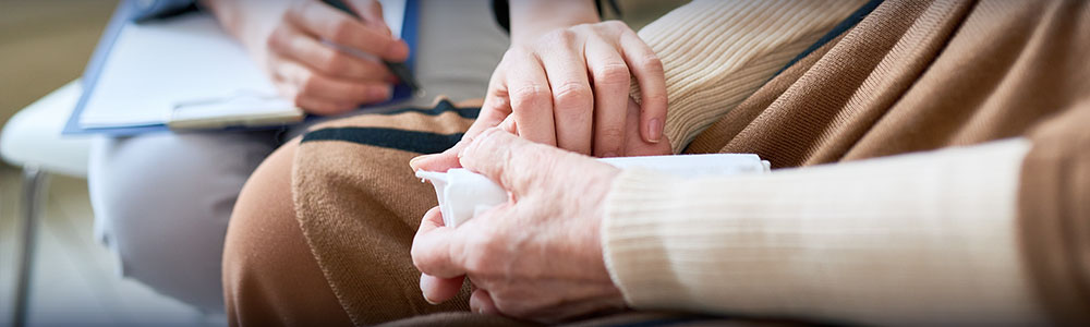 counselor providing comfort to a grieving person by holding one of their hands cupped in their lap