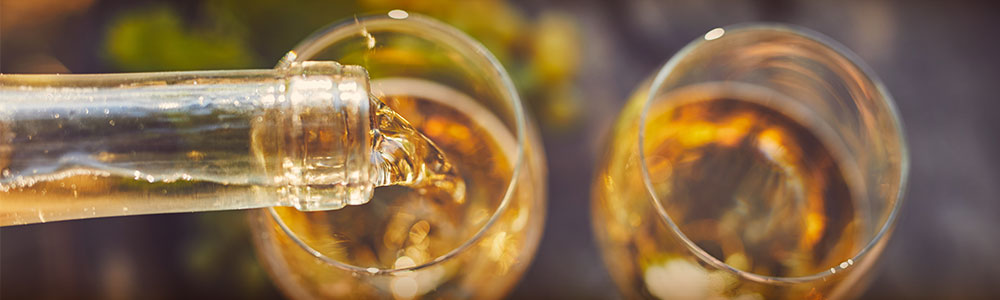 overhead shot of glasses being filled with white wine from a bottle