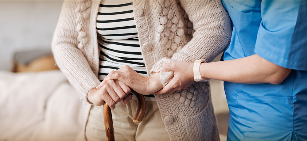 Woman with cane helped by nurse in her home.