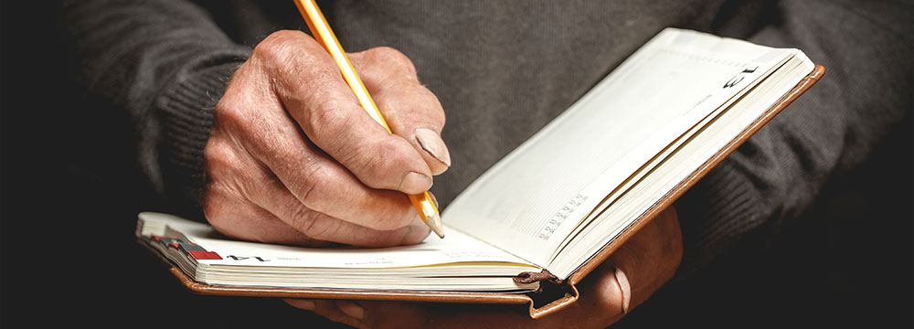 closeup up of man writing in a book he is holding