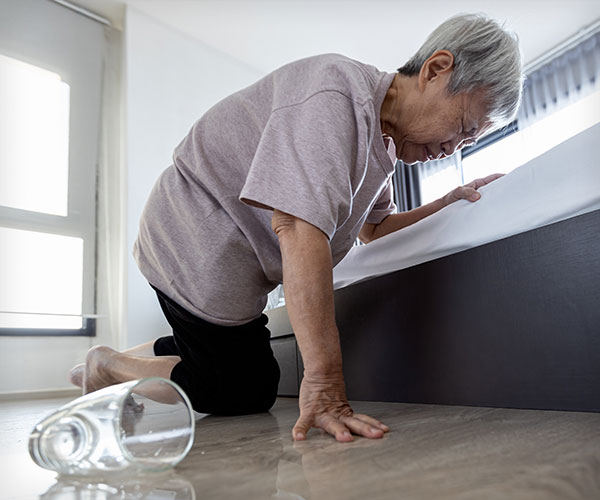 dizzy woman crouching next to her bed with a dropped cup on the floor