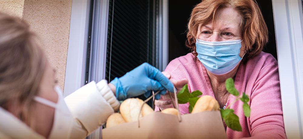 masked woman delivering groceries to homebound woman