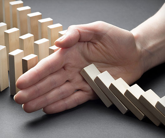 Close-up of a businessman hand stopping a falling domino effect of risk, crisis.
