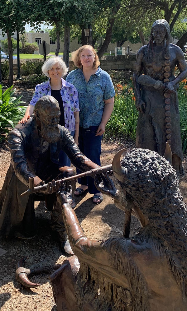 Visitors posing with bronze statues in the Rose Garden area of Fredericksburg’s MarktPlatz commemorating John O. Meusebach and Comanche Chief Santanna sharing a peace pipe.