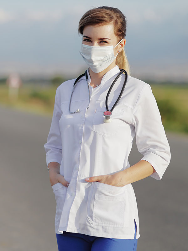 Female doctor or nurse wearing a protective face mask next to a rural road.