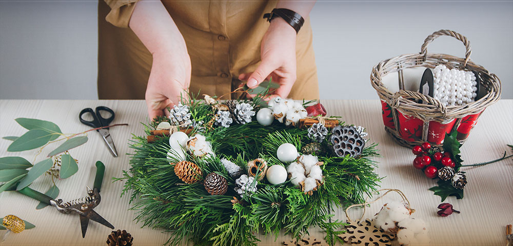  Closeup of hands assembling a wreath on a table with tools and materials.