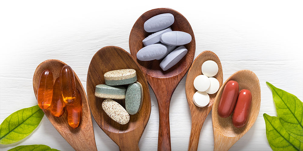 Assorted pills sorted in different wooden spoons on white table with leaves.