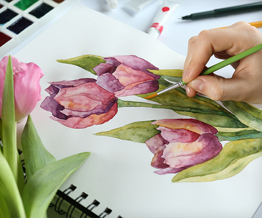 Closeup of hands painting tulips on the table in a notebook with watercolor.