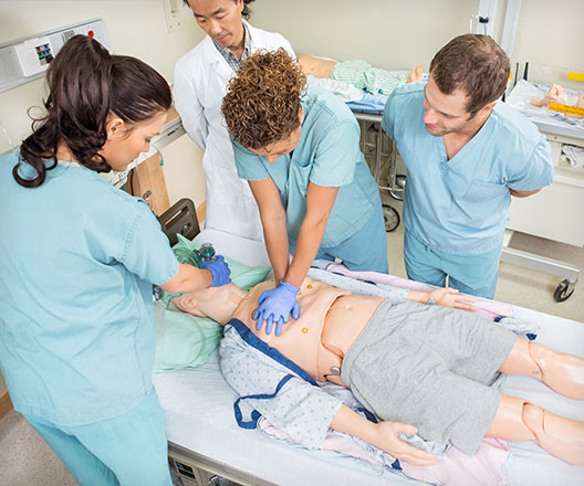 Nurses performing CPR on a dummy patient while a doctor stands by in a hospital room.