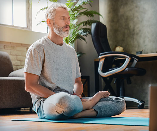 Man meditating on mat in home.