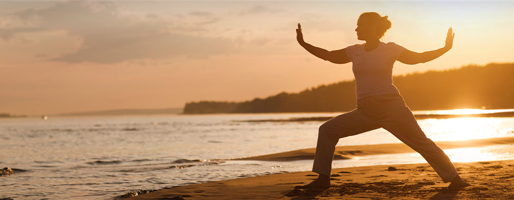 Woman practicing tai chi chuan at sunset on the beach.