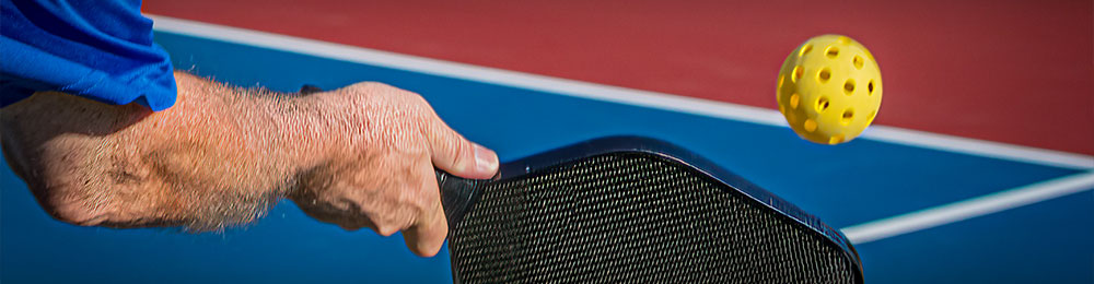 Arm of man hitting a pickleball with a paddle.