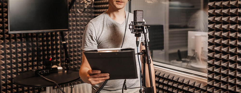  Man with script behind mic in recording studio.
