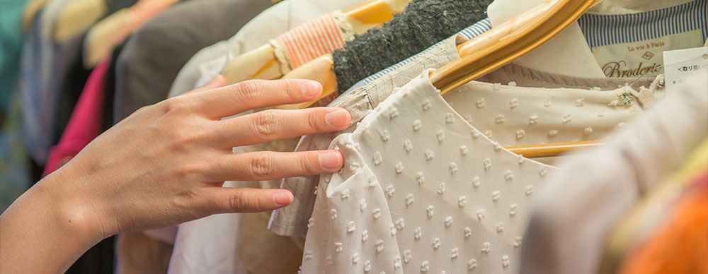  Closeup of a woman's hand perusing clothes hanging on the sales rack.