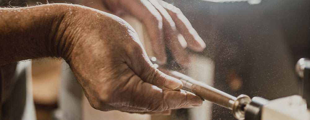 Close up of hands crafting a wooden pen on a lathe.