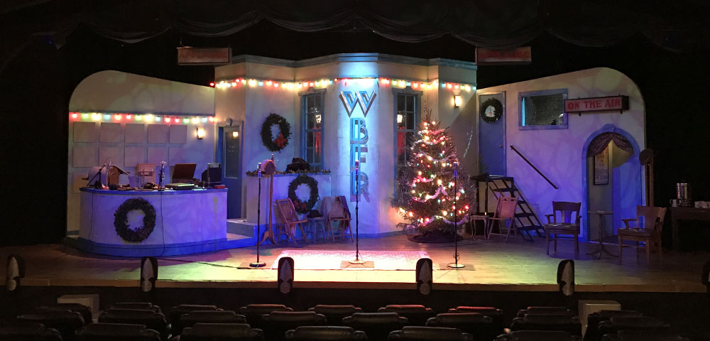 A lit radio station set with three mic stands on the stage at the Fredericksburg Theater Company.