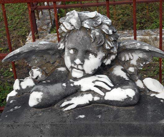 Stone monument of cherub resting chin on folded arms .