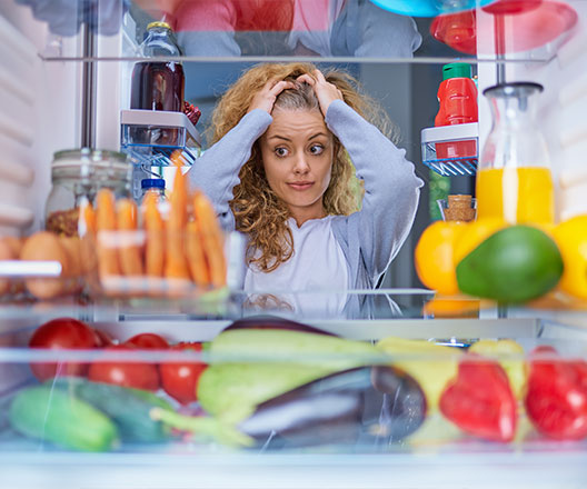 Anxious woman looking at food in a fridge.