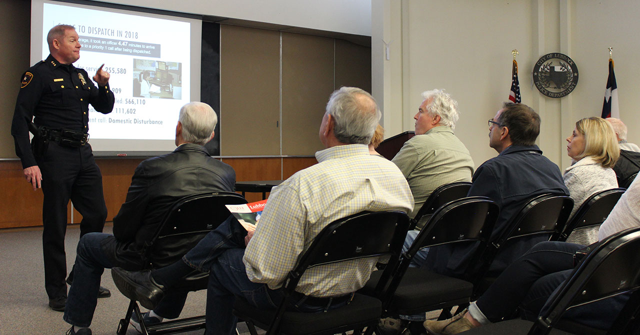 Police Chief Greg Stevens presents to OLLI members. Greg Stevens stands at the front of a classroom in front of a projector screen and points his index finger into the attentive audience.