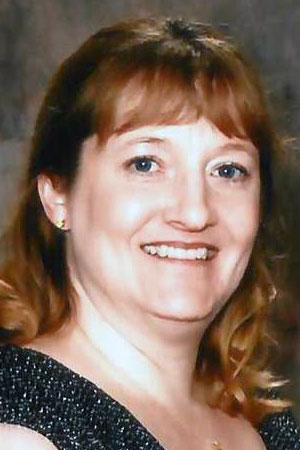 A headshot of Misha Price. Misha poses for a headshot while smiling and wearing a earrings, a necklace and a dark colored shirt.