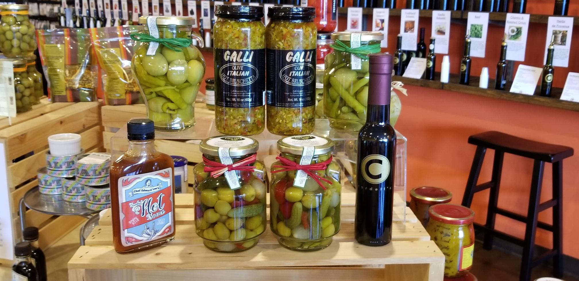 Products featured at Cordell's A variety of Cordell's products including wine, peppers and canned salt sitting atop wooden crates with other wine bottles displayed in the background.