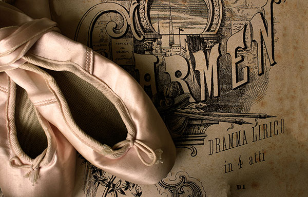 A pair of light-pink colored ballet shoes are stacked together on top of a playbill for the performance of Carmen