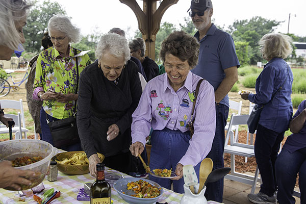 OLLI members enjoy a meal outside at ThistleDew Lavender Farm. OLLI members stand behind one another in a line as they scoop servings of food from a table onto their plates.
