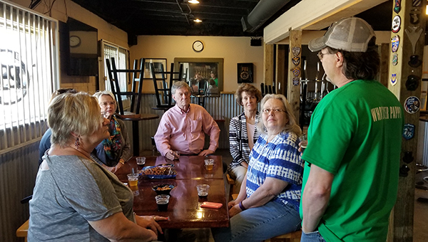 OLLI memebers sit around a long table and attentively look up at a speaker wearing a green shirt.