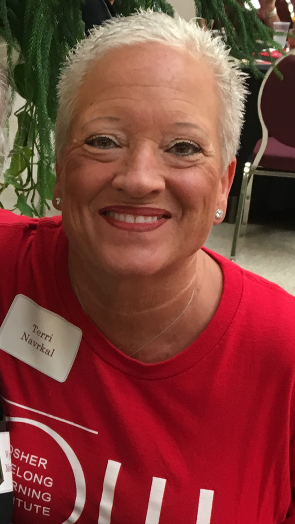 Terri sits while smiling and wearing stud earrings and a red-colored OLLI shirt