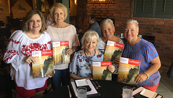 Terri holds a OLLI Lubbock brochure while standing alongside other OLLI members who do the same inside a restaurant near a table.