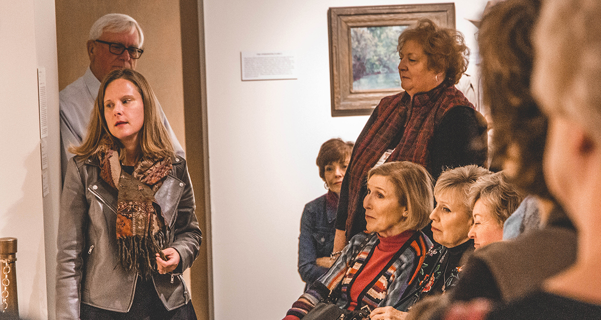 Amy Von Lintel stands to the left of her audience and looks to her right as the audience looks in the same direction while seated.