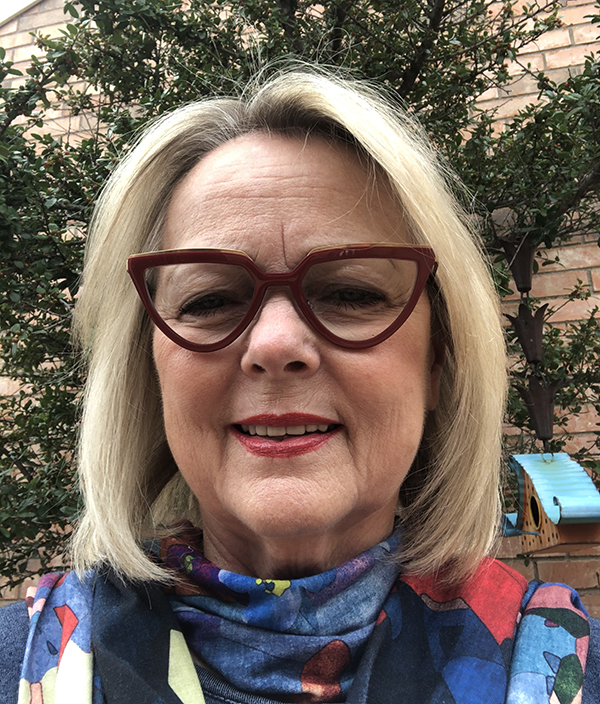 Susan Robinson A headshot of Susan Robinson smiling while wearing scarlet colored glasses and a multi-colored scarf while standing outside