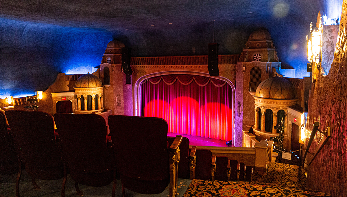 Rows of seats descend inside of a large room with various colors and a stage