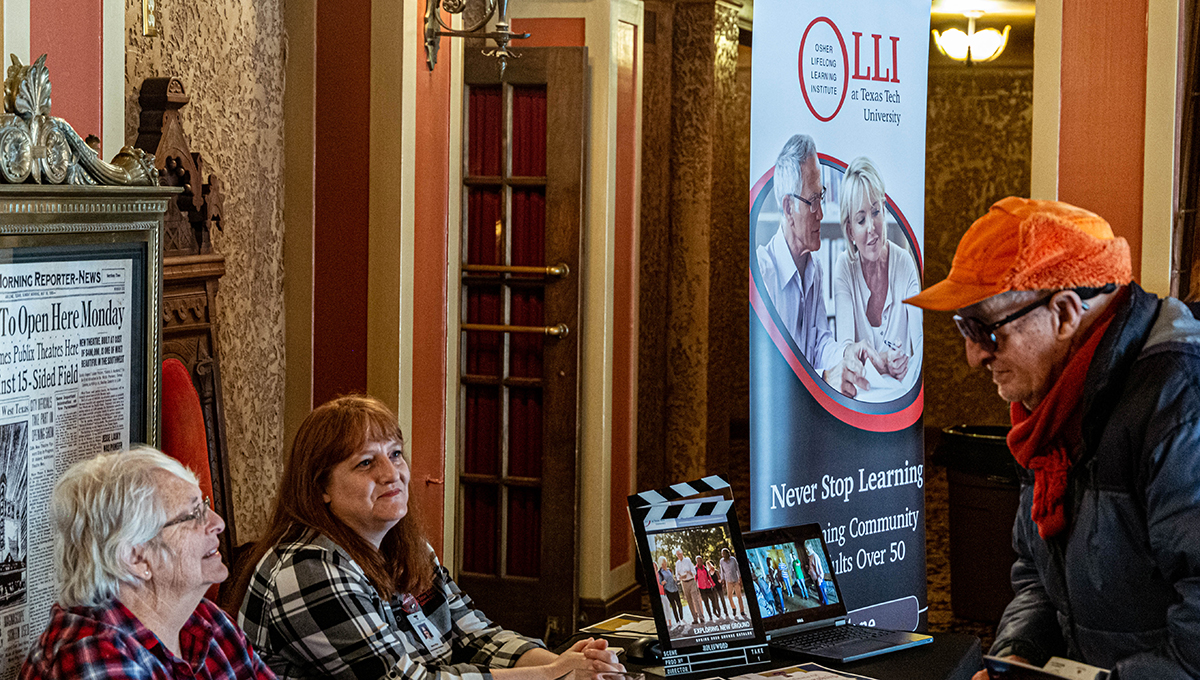 OLLI Coordinator, Misha Price and OLLI volunteer, Barbara Shaw speak with a Paramount Theatre patron Rows of seats descend inside of a large room with various colors and a stage