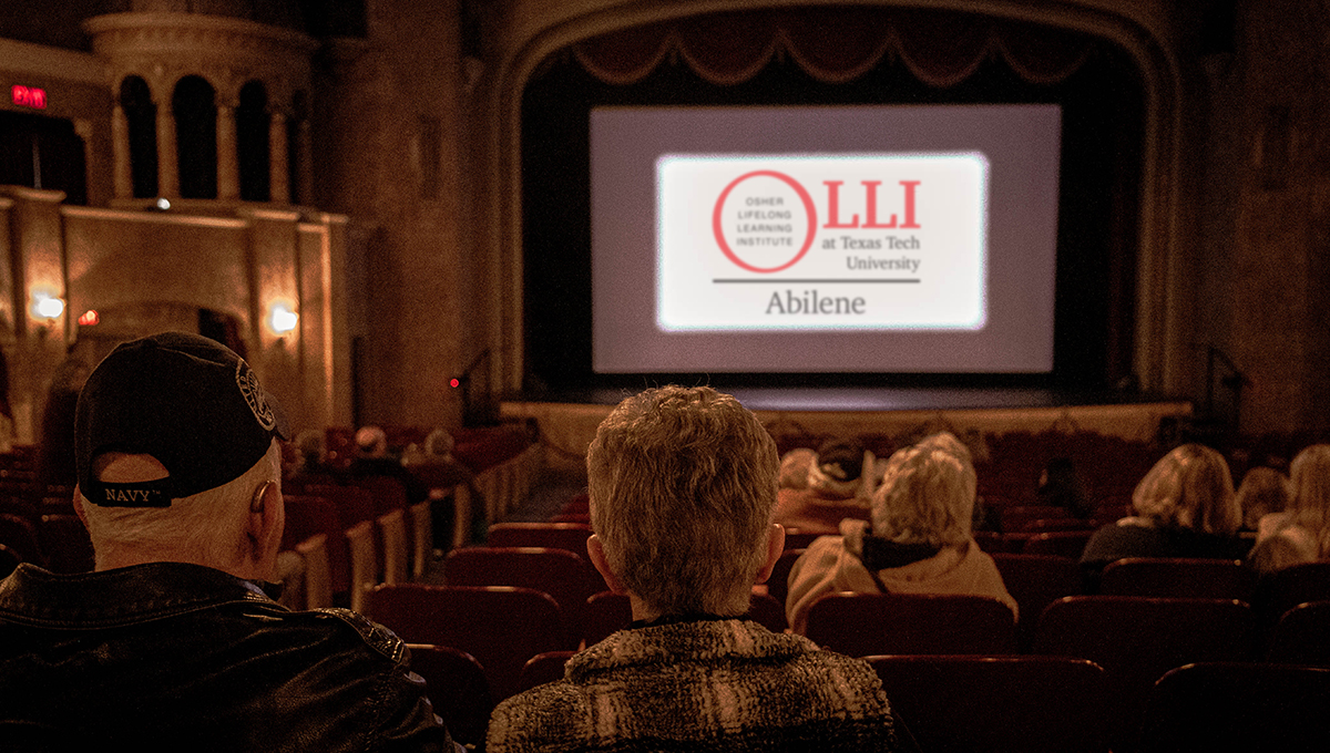 Rows of seats descend inside of a large room with various colors and a stage