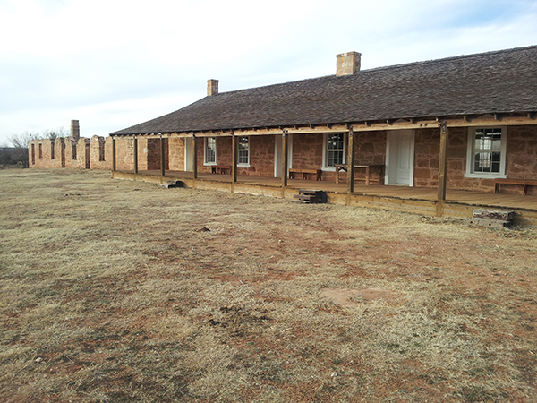 Fort Chadbourne Barracks A home with numerous windows and doors rests behind dry grass.