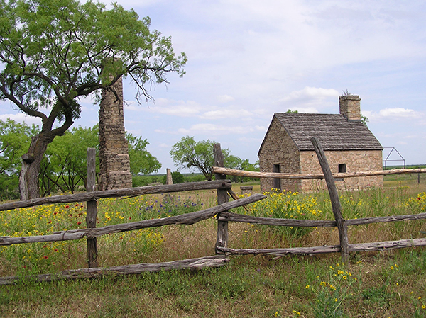 Fort Phantom Hill A small roofed building rests in a field with green grass and a wooden fence enclosure.
