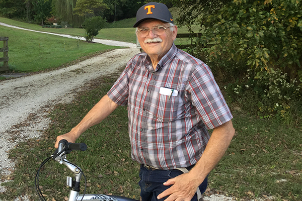 OLLI instructor Fred Bailey An older man wearing glasses and a plaid shirt stands outdoors with a path and greenery in the background