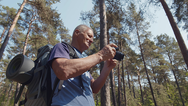 Photography can be for everyone. A stock graphic of an older man wearing a backpack and holding a camera while looking down.